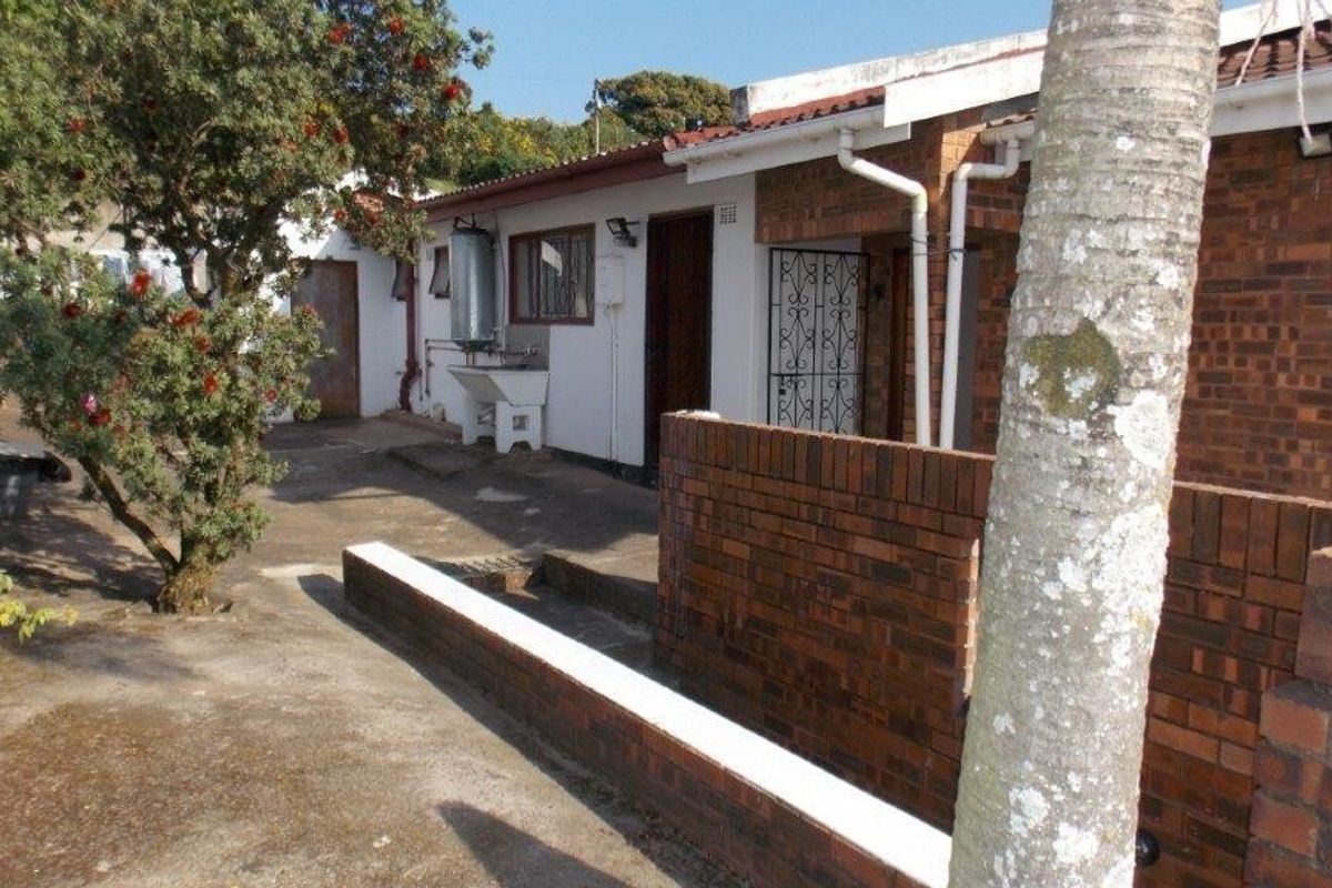 Rear exterior view of the property featuring brick construction, concrete paving, and an external utility area with a sink and geyser.