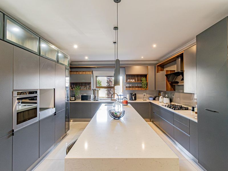 Modern kitchen featuring a large central island with quartz countertops, sleek grey cabinetry, built-in appliances, and contemporary pendant lighting.