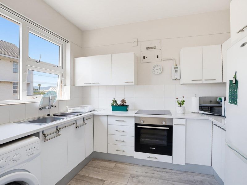 A functional kitchen featuring white cabinetry, built-in oven, electric cooktop, tiled splashback, and space for a washing machine.