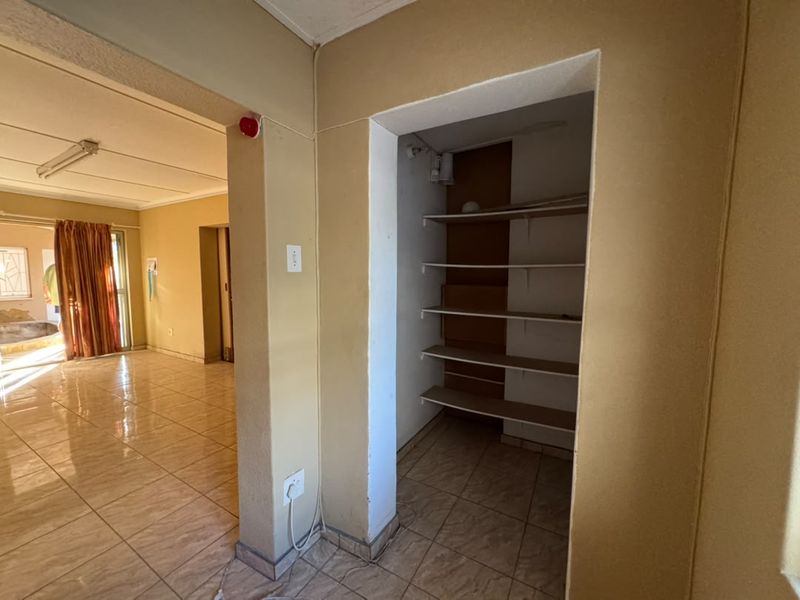 A functional scullery or pantry area featuring built-in shelving and tiled flooring, adjacent to the main living space.