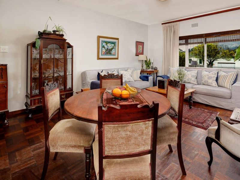 An open-plan living and dining area featuring classic parquet flooring and a large window that provides natural light.