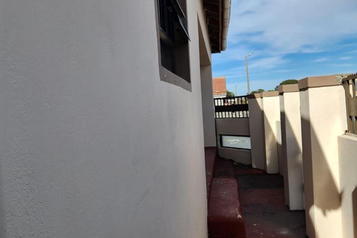 A narrow exterior side passage featuring a painted concrete walkway and masonry boundary wall.