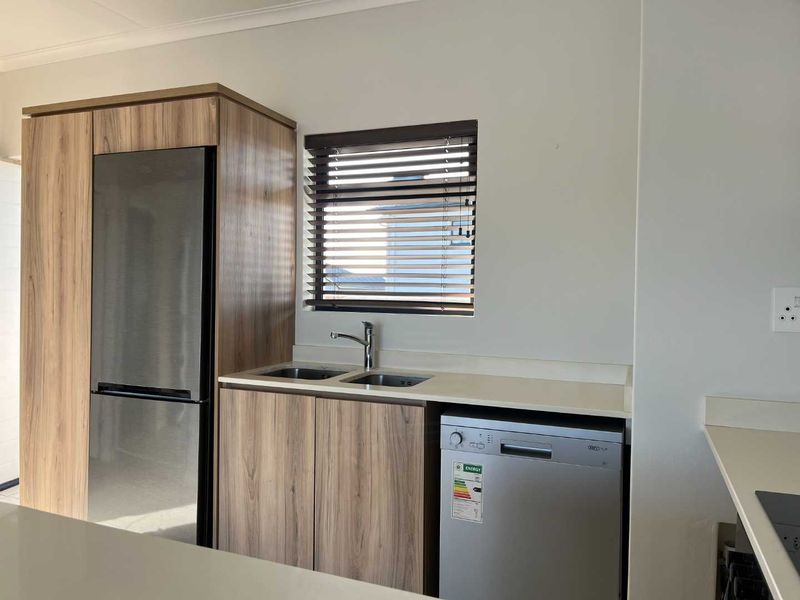 A functional scullery area featuring modern wood-finish cabinetry, a double sink, and a countertop, providing efficient workspace and storage.
