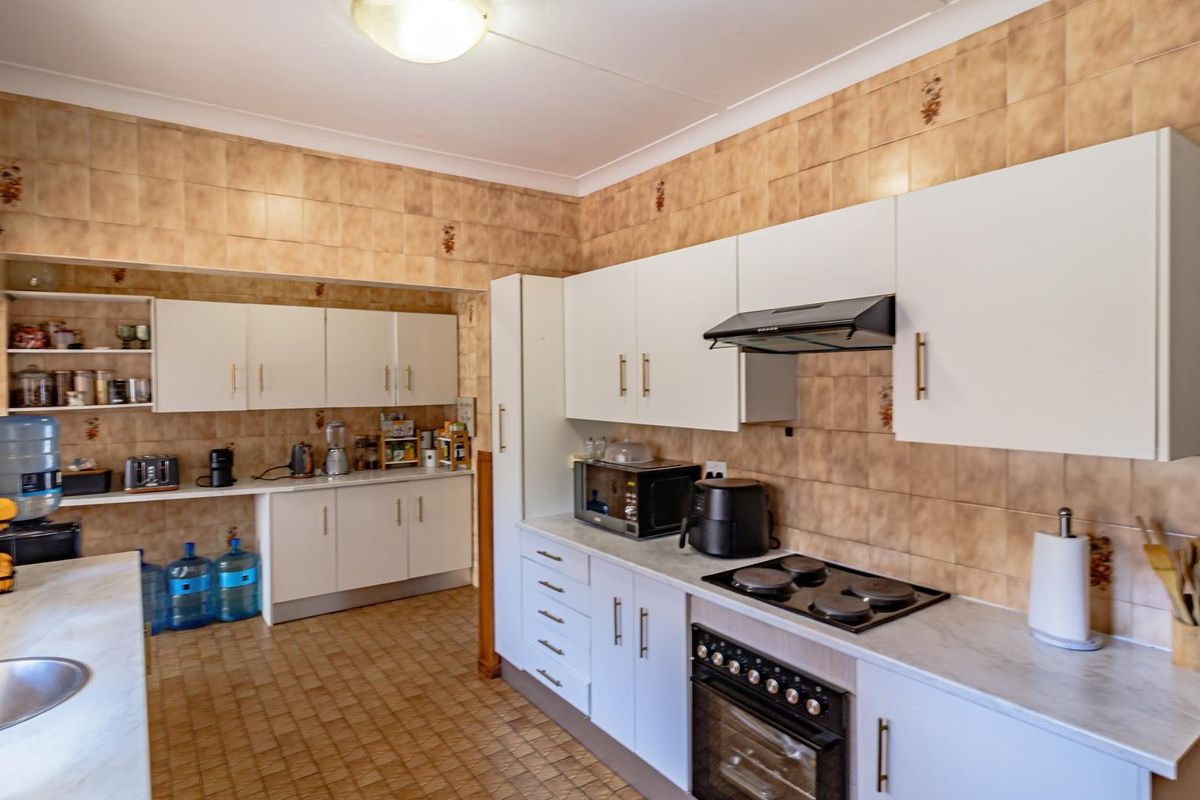 A functional kitchen featuring white cabinetry, built-in oven, electric hob, extractor fan, and ample counter space with tiled walls and flooring.