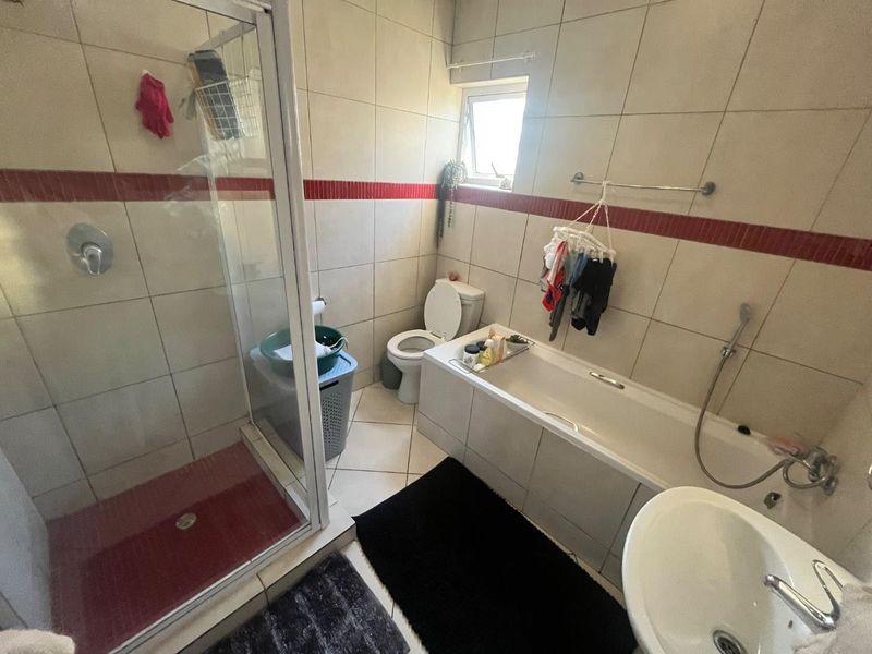 A functional bathroom featuring a shower enclosure, bathtub, toilet, and washbasin with tiled finishes and a small window for natural light.