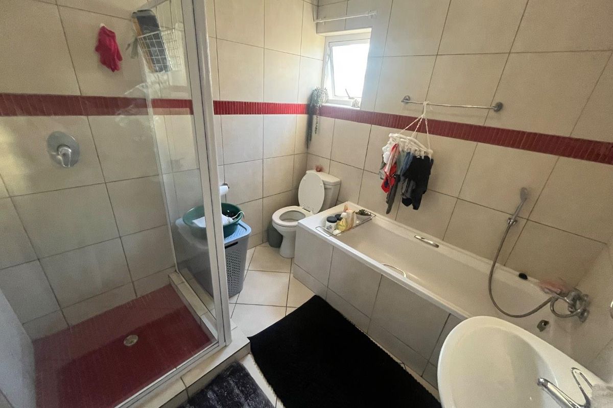A functional bathroom featuring a shower enclosure, bathtub, toilet, and washbasin with tiled finishes and a small window for natural light.