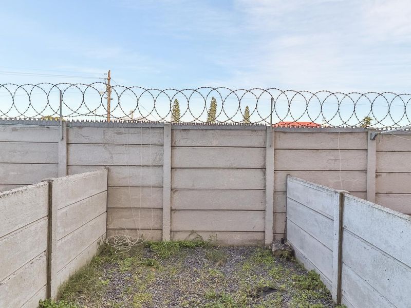 A rear exterior area featuring a precast concrete boundary wall topped with razor wire and a gravel-surfaced ground.