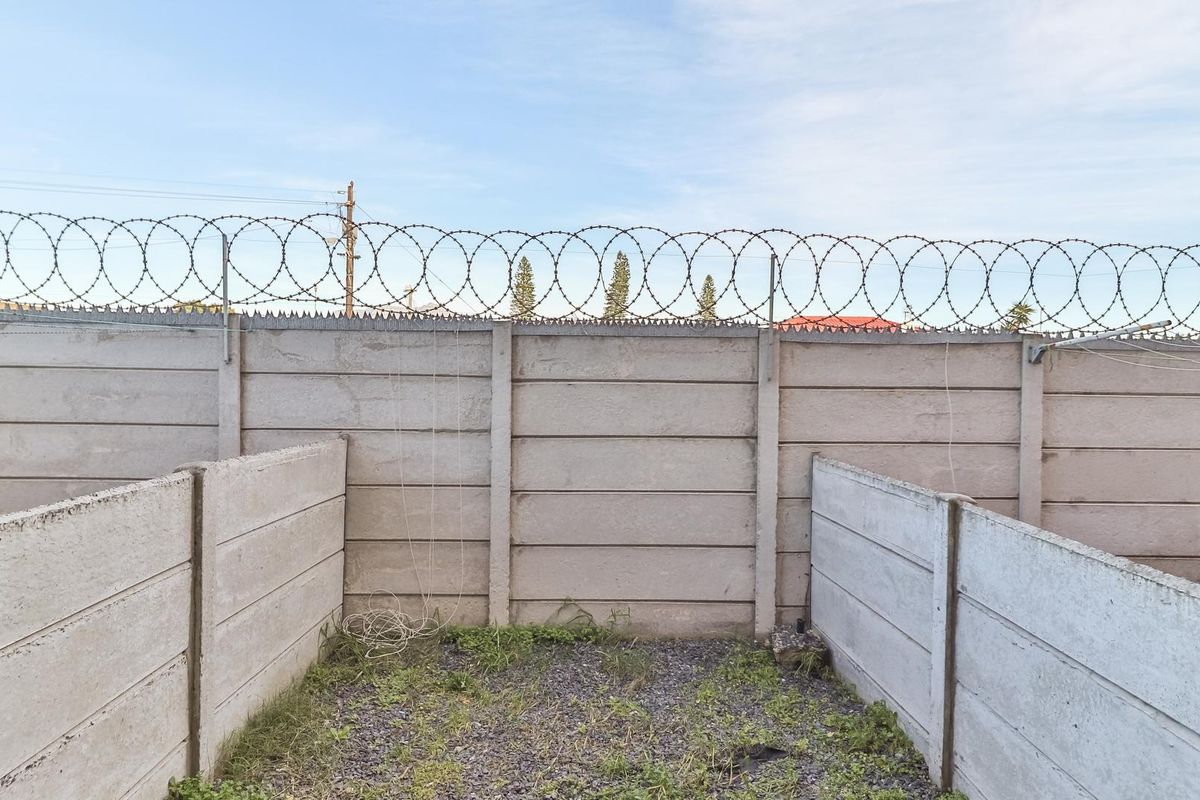 A rear exterior area featuring a precast concrete boundary wall topped with razor wire and a gravel-surfaced ground.