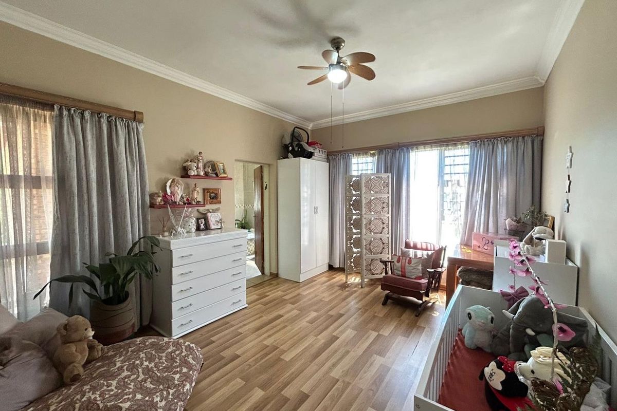 A spacious bedroom featuring wood-look laminate flooring, crown molding, and a ceiling fan, with large windows providing ample natural light.