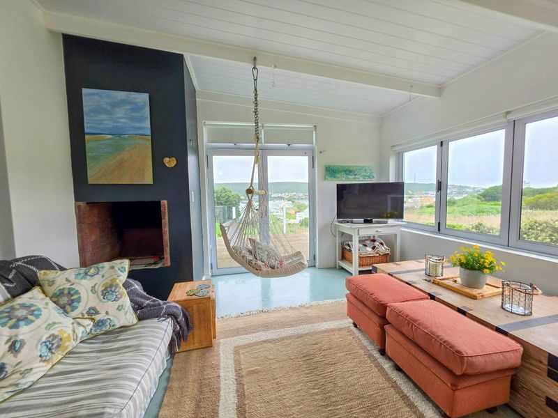 A bright living room featuring an exposed beam ceiling, a built-in fireplace, and large windows offering scenic views with access to an outdoor area.