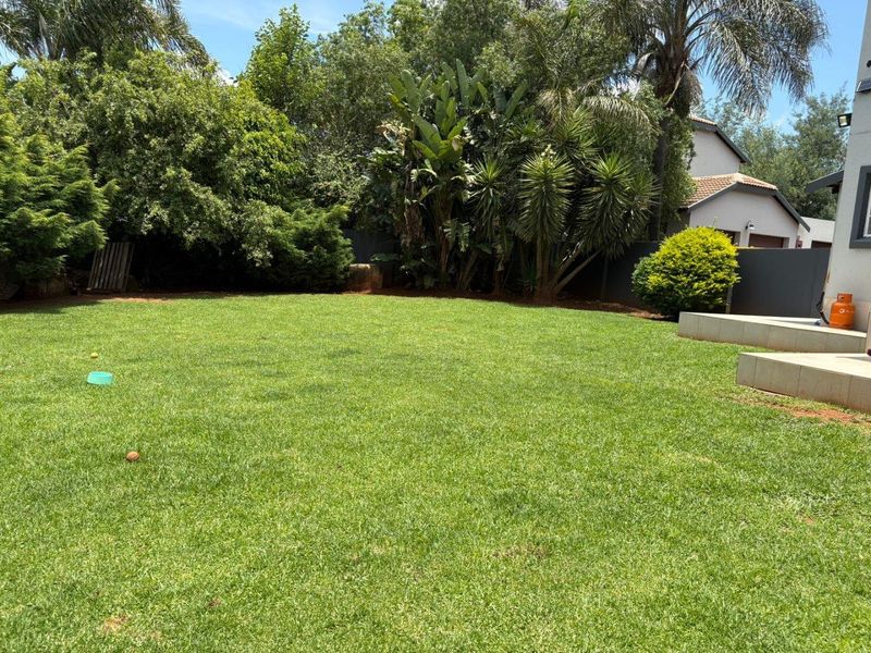 A well-maintained private garden featuring a lush green lawn, mature perimeter landscaping, and paved patio steps leading to the residence.
