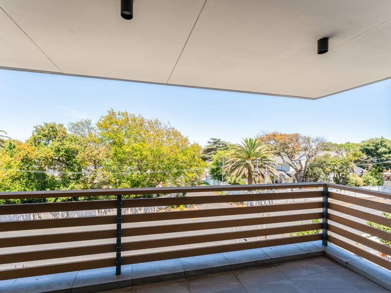 A modern, covered balcony featuring tiled flooring, sleek slatted timber railings, and recessed ceiling lighting, offering a pleasant elevated view of the surrounding neighborhood.