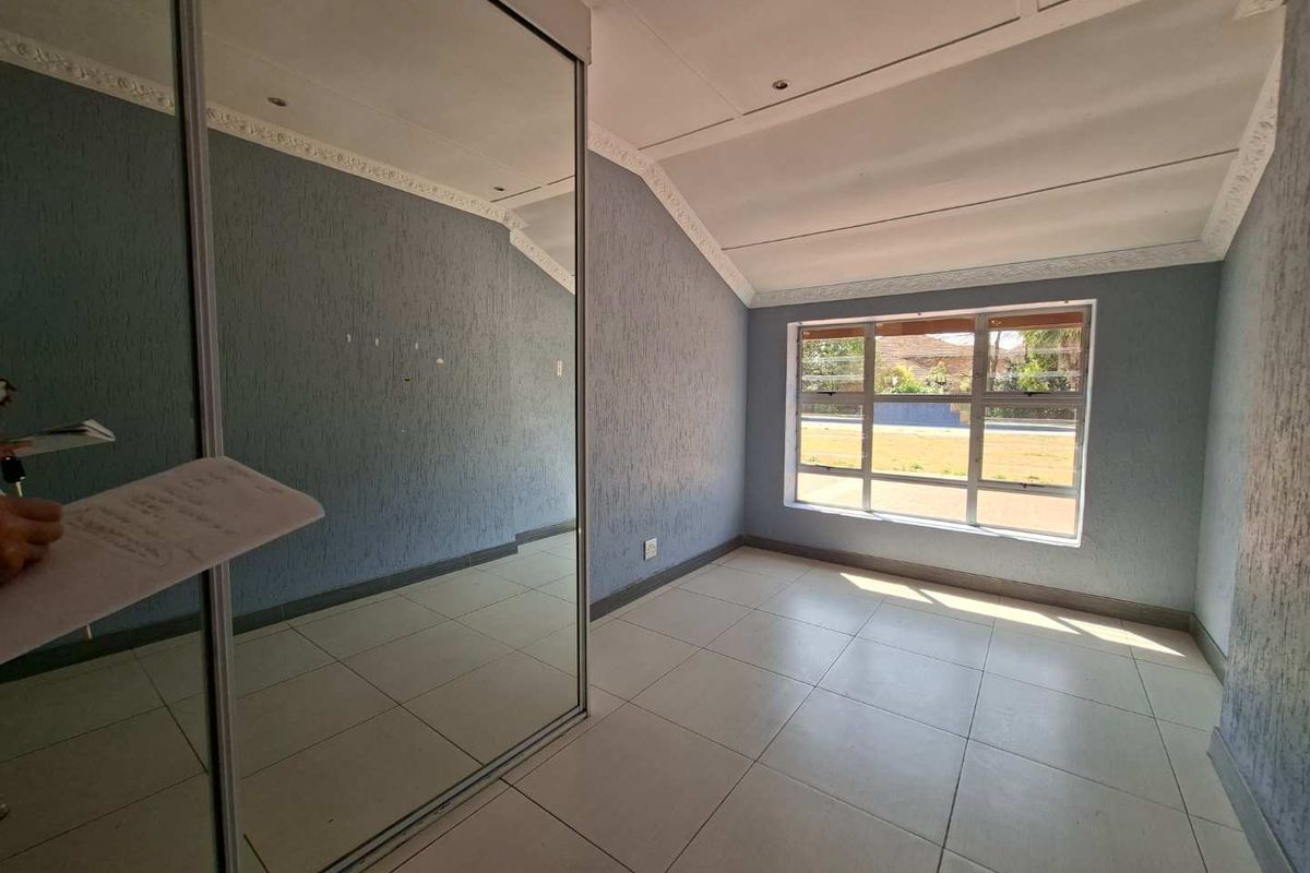 A bright, empty bedroom featuring tiled flooring, a large window, and a spacious built-in mirrored wardrobe.