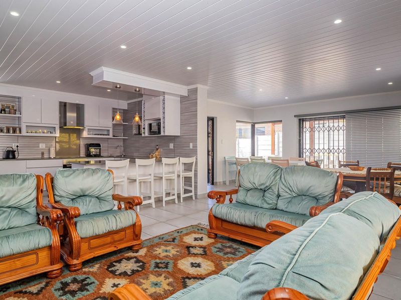 Spacious open-plan living area featuring a modern kitchen with island, stone feature wall, and recessed lighting, seamlessly connecting to the dining and lounge spaces.