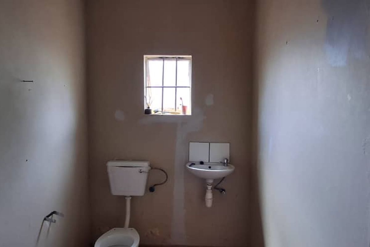 A small, dated bathroom featuring a basic toilet and wall-mounted basin, requiring cosmetic updates and wall repairs.
