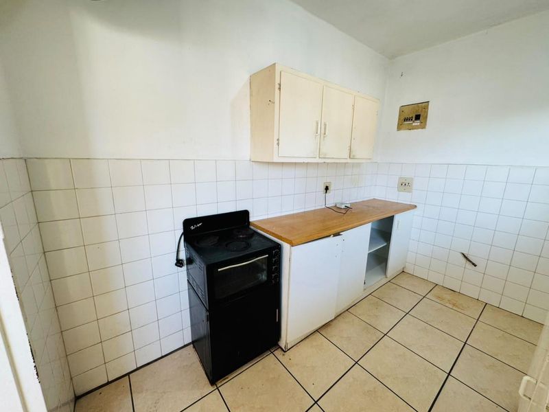 A compact, dated kitchen featuring basic cabinetry, a tiled splashback, and ceramic flooring, offering a blank canvas for a modern renovation.