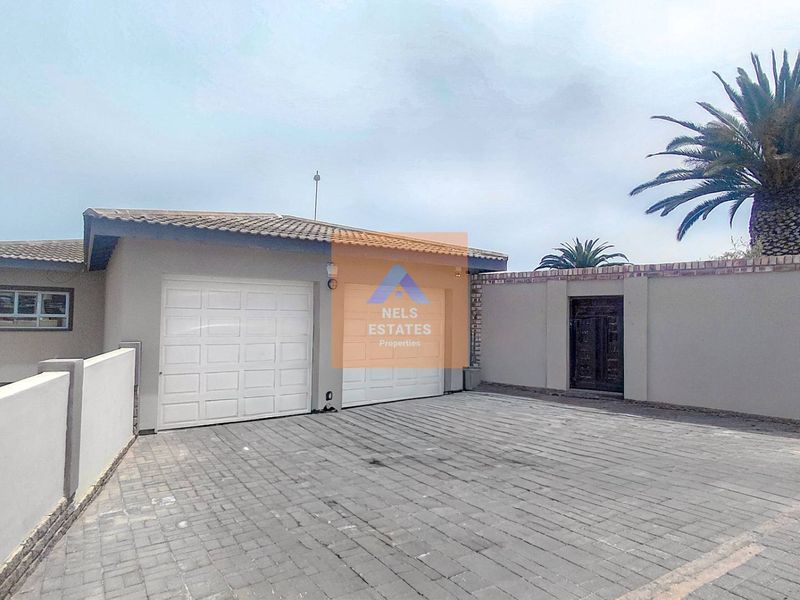 Front exterior view of the property featuring a double garage, paved driveway, and secure boundary walling.