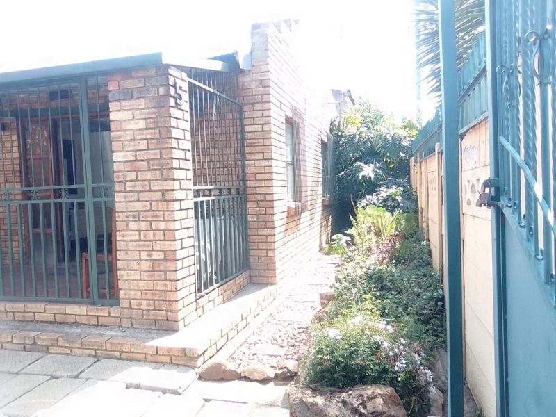 A view of the property's face brick exterior, featuring a secure entrance with metal security gates and a paved walkway alongside a garden area.
