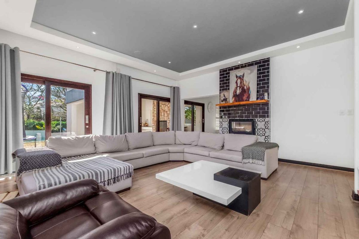 Spacious living room featuring a modern recessed ceiling, timber flooring, and a striking tiled fireplace, with direct access to the outdoor area.