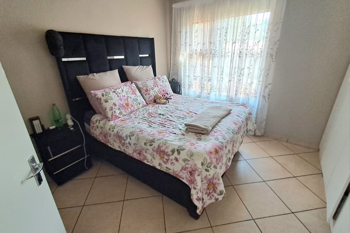 A functional bedroom featuring tiled flooring, built-in cupboards, and a large window with natural light, providing a comfortable and practical living space.