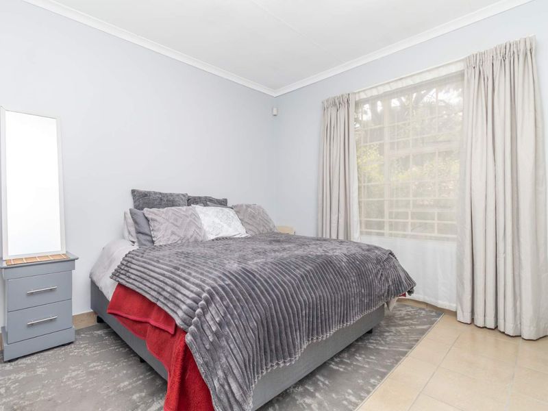 A well-maintained bedroom featuring tiled flooring, coved ceilings, and a window fitted with security bars, offering a clean and functional living space.