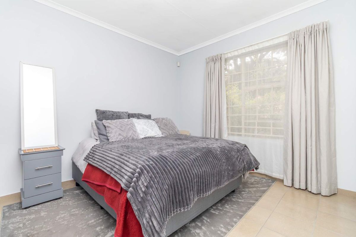 A well-maintained bedroom featuring tiled flooring, coved ceilings, and a window fitted with security bars, offering a clean and functional living space.