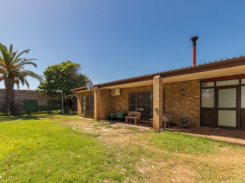 Rear view of the house featuring a brick facade, covered patio area, and a spacious garden with established palm tree.