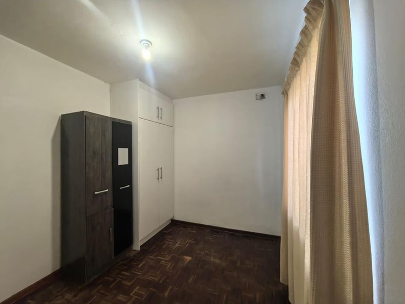 A bright bedroom featuring classic parquet flooring and ample built-in cupboard storage, offering a clean and functional space ready for personalization.