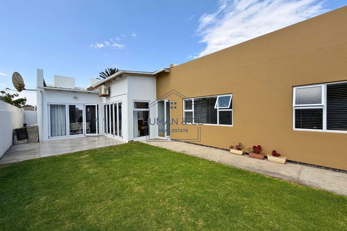 Rear view of the property featuring a well-maintained lawn, tiled patio area, and multiple sliding glass doors providing access to the interior.