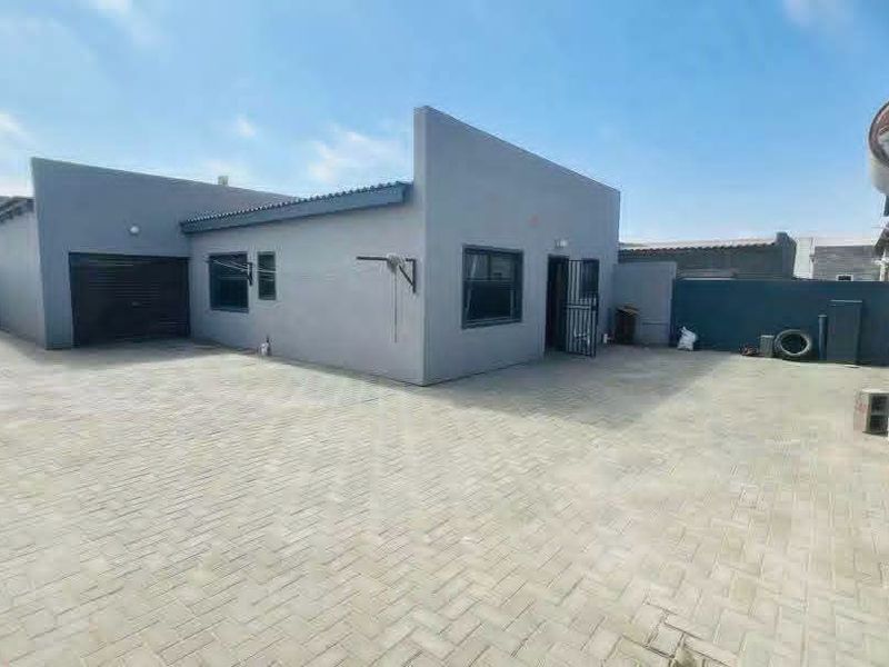 A spacious paved rear courtyard area featuring a garage entrance, secure access door, and perimeter boundary walls.