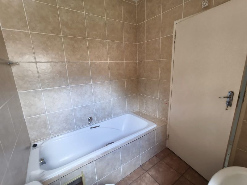 A functional bathroom featuring a built-in bathtub with neutral ceramic wall and floor tiling.