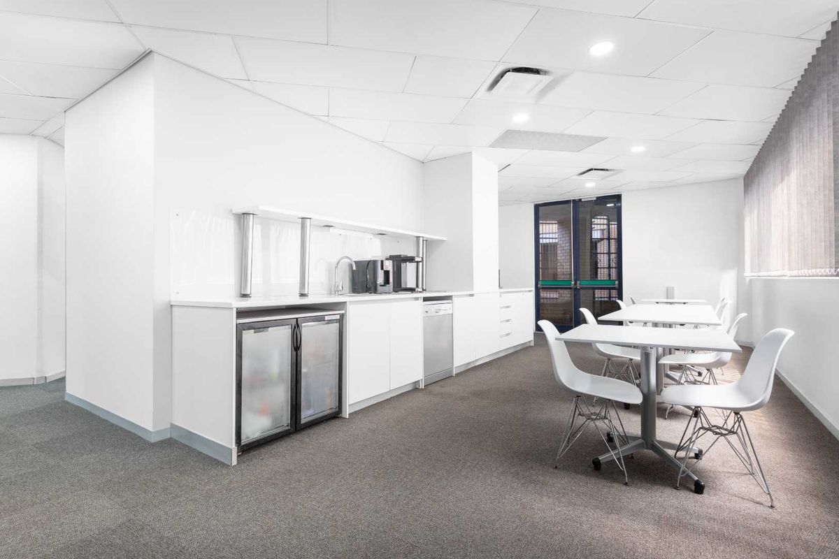 A bright office kitchenette area featuring white cabinetry, a stainless steel sink, integrated under-counter refrigeration, and a dishwasher, set within a professional workspace.