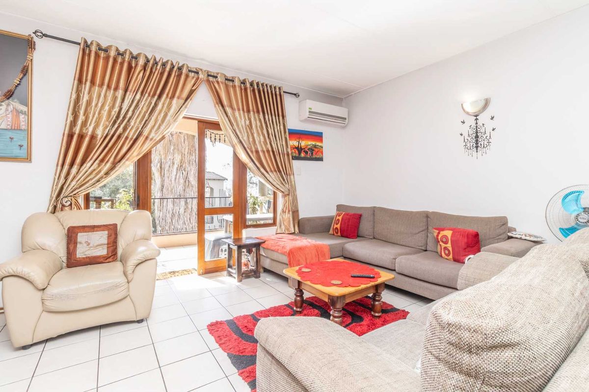 A bright living room featuring tiled flooring, a wall-mounted air conditioning unit, and direct access to an outdoor balcony through a sliding glass door.