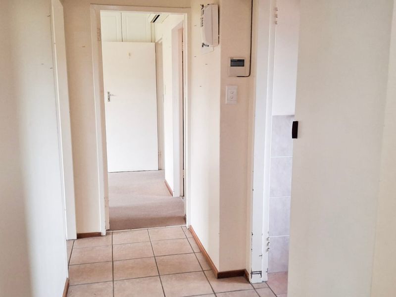 A functional hallway connecting multiple rooms, featuring a mix of tiled and carpeted flooring with neutral wall finishes.