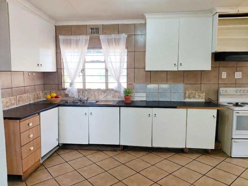 A functional kitchen featuring white cabinetry, dark laminate countertops, tiled splashbacks, and a freestanding stove, offering potential for modern cosmetic updates.
