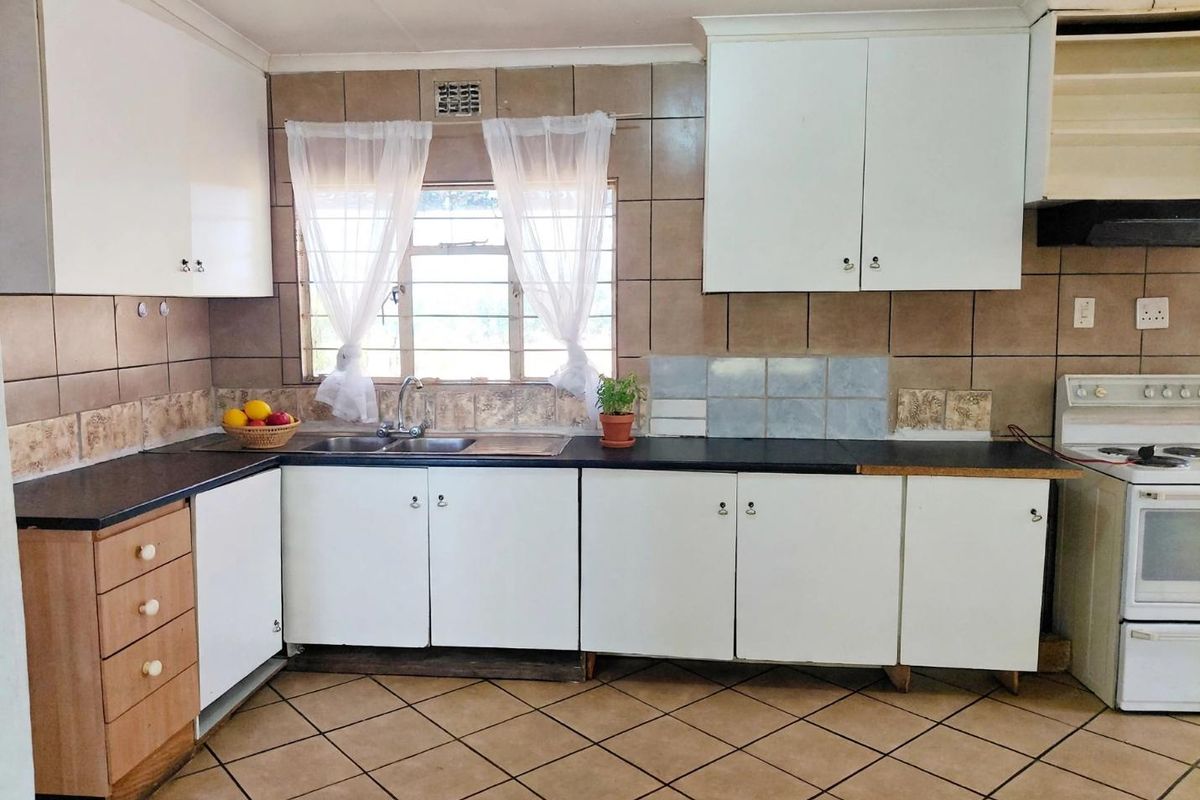 A functional kitchen featuring white cabinetry, dark laminate countertops, tiled splashbacks, and a freestanding stove, offering potential for modern cosmetic updates.