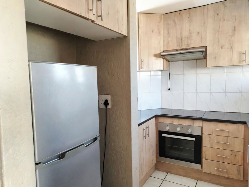 Compact kitchen featuring light wood-finish cabinetry, dark countertops, built-in oven, electric hob, and tiled splashback.