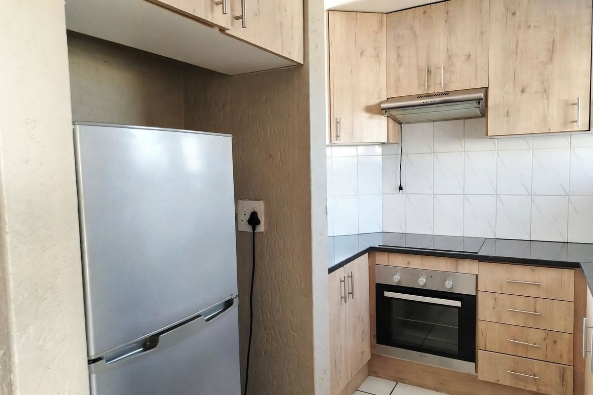 Compact kitchen featuring light wood-finish cabinetry, dark countertops, built-in oven, electric hob, and tiled splashback.