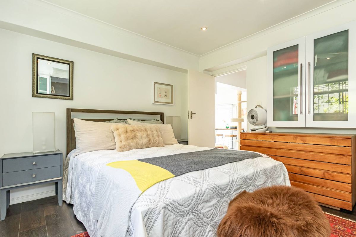 A well-maintained bedroom featuring dark wood-look flooring, recessed ceiling lighting, and a built-in wall cabinet with glass-panel doors.