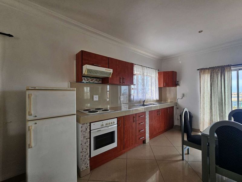 A functional kitchen featuring wood-finish cabinetry, tiled flooring, a built-in oven with electric hob, and a tiled backsplash.