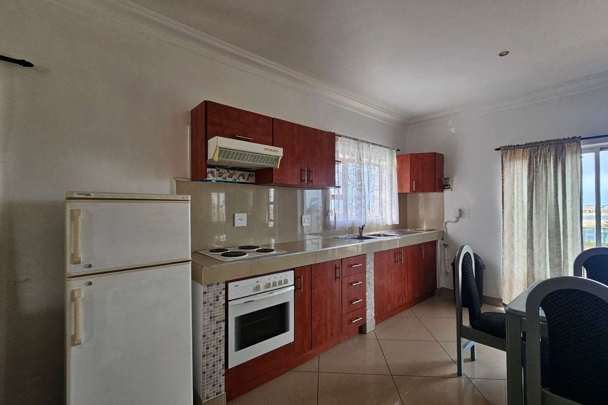 A functional kitchen featuring wood-finish cabinetry, tiled flooring, a built-in oven with electric hob, and a tiled backsplash.