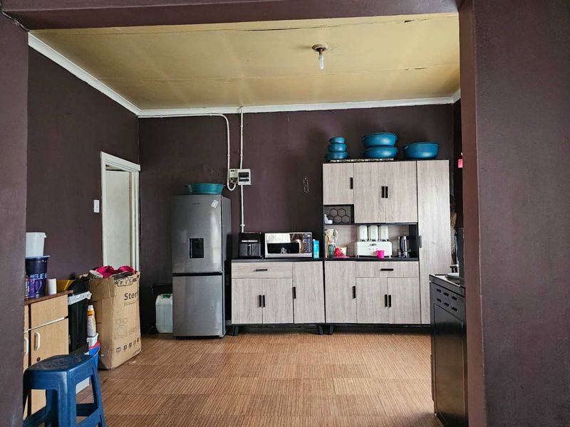 A functional kitchen area featuring light wood-finish cabinetry, dark painted walls, and laminate flooring, requiring some cosmetic updates to the ceiling and electrical finishes.