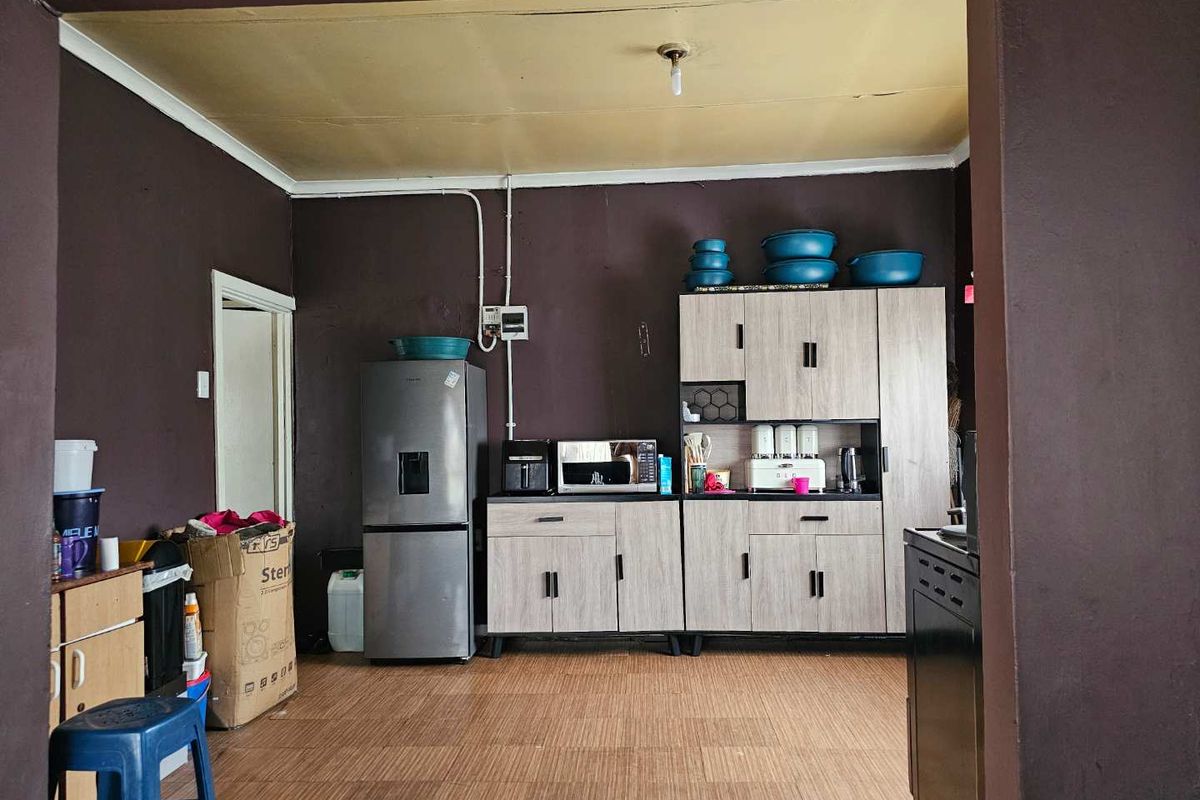 A functional kitchen area featuring light wood-finish cabinetry, dark painted walls, and laminate flooring, requiring some cosmetic updates to the ceiling and electrical finishes.