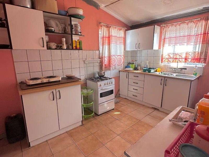 A functional kitchen featuring white cabinetry, a gas stove, tiled backsplash, and tiled flooring, requiring cosmetic updates to modernize the space.