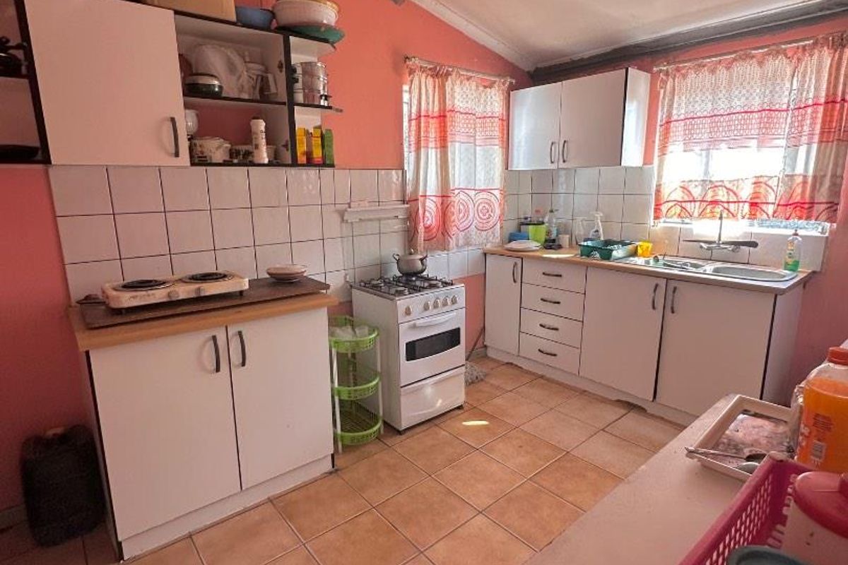 A functional kitchen featuring white cabinetry, a gas stove, tiled backsplash, and tiled flooring, requiring cosmetic updates to modernize the space.