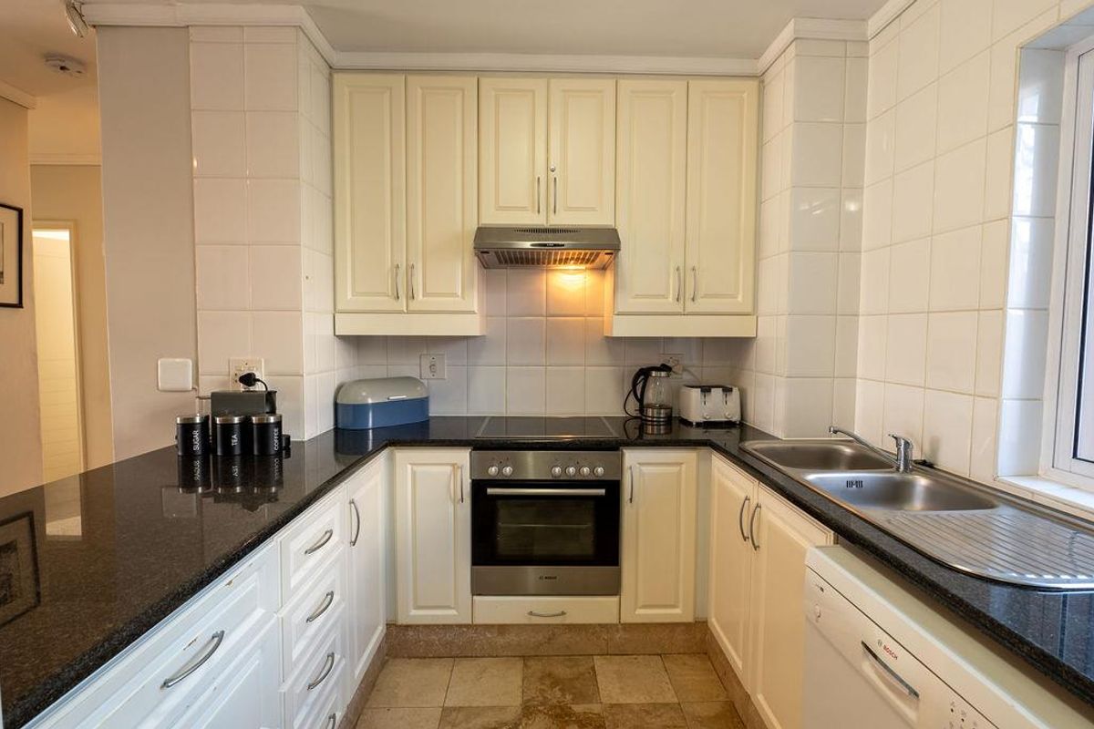 A functional U-shaped kitchen featuring cream cabinetry, dark granite countertops, a built-in oven, extractor fan, and a stainless steel double sink.