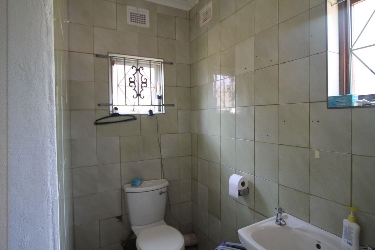A dated bathroom featuring wall-to-wall ceramic tiling, a standard toilet, and a wall-mounted basin with security bars on the window.