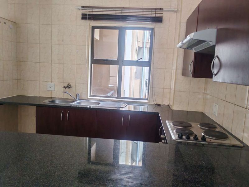 A functional kitchen featuring dark wood cabinetry, granite countertops, a built-in electric hob with extractor fan, and a stainless steel sink.