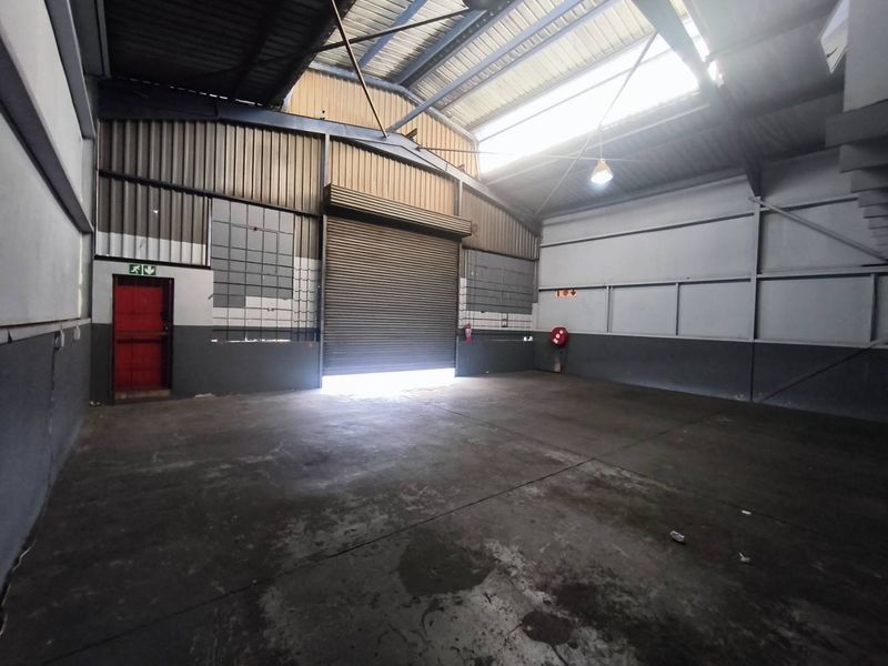 Spacious industrial warehouse unit featuring high ceilings with exposed steel trusses, a large roller shutter door, and durable concrete flooring.