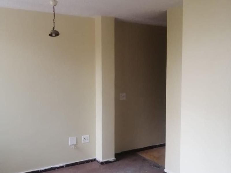 An empty living room space featuring neutral walls, a pendant light fixture, and worn flooring, ready for renovation or staging.